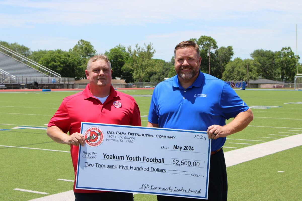 Chad Ledlow stands with a representative from Yoakum Youth Football and presents a $2,500 check.