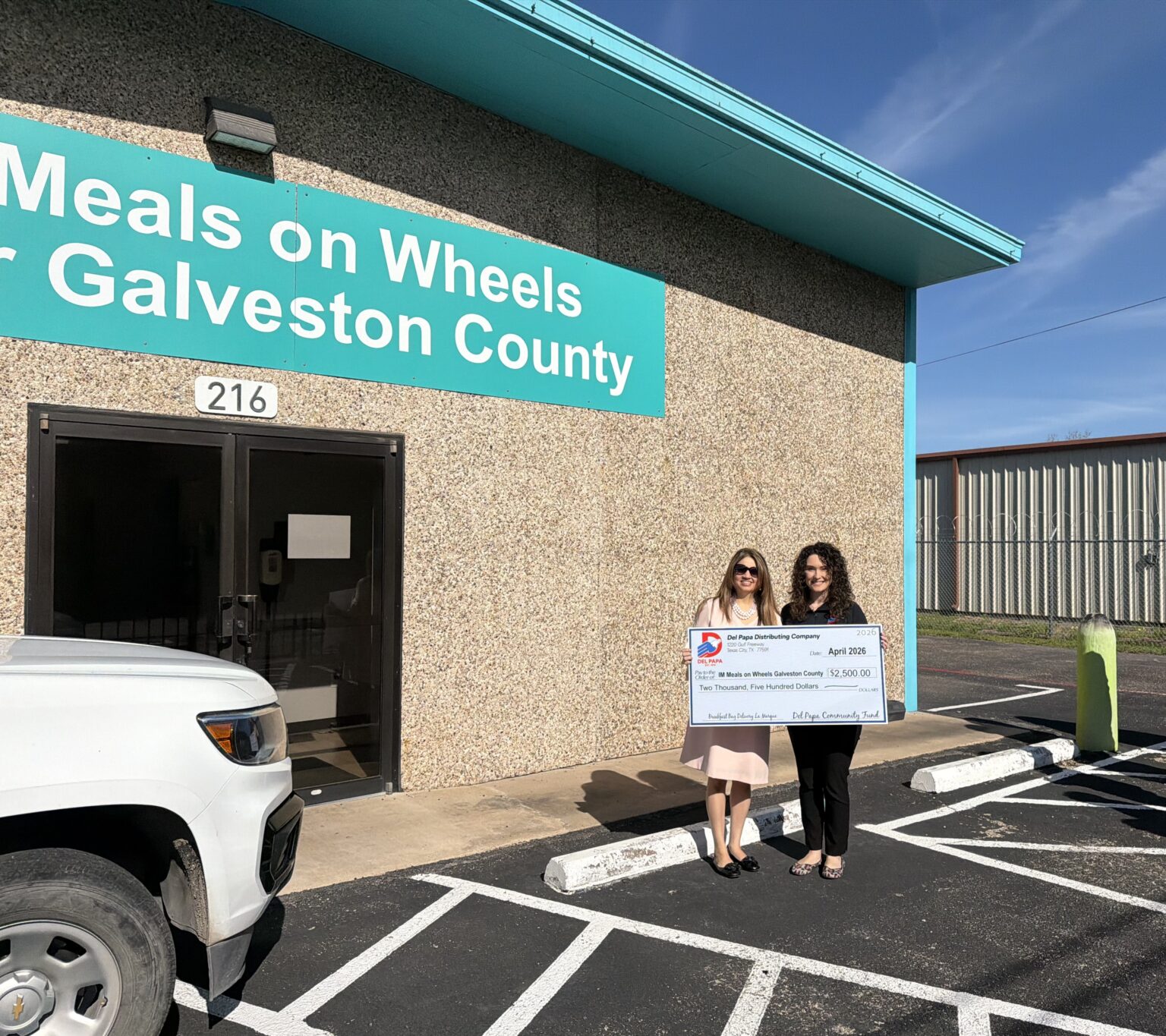 Emily presents a check to Meals on Wheels of Galveston County in front of their building.